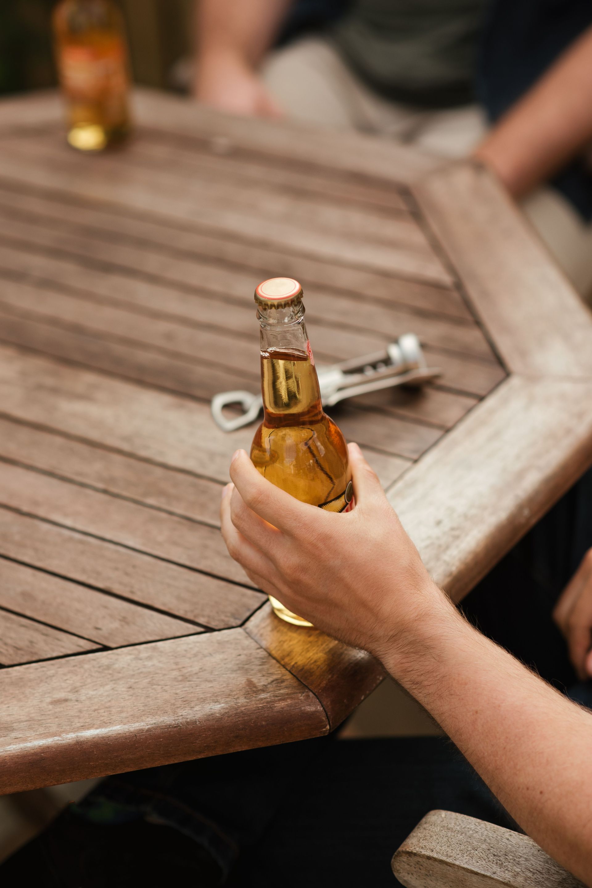 From above of crop anonymous male spending weekend with friend at table with bottle of beer in yard