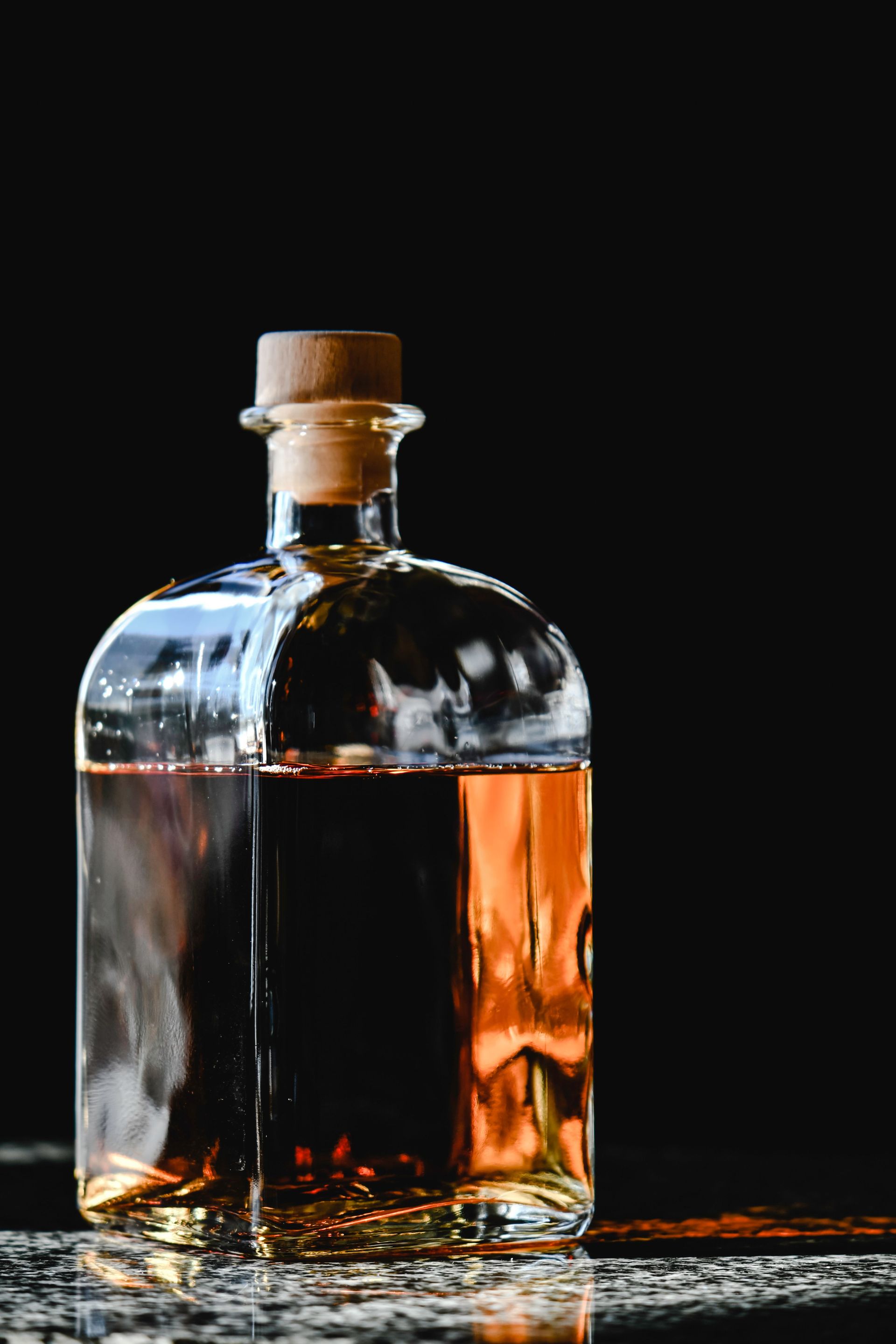 A stylish glass bottle of whiskey with cork stopper against a dramatic black backdrop.