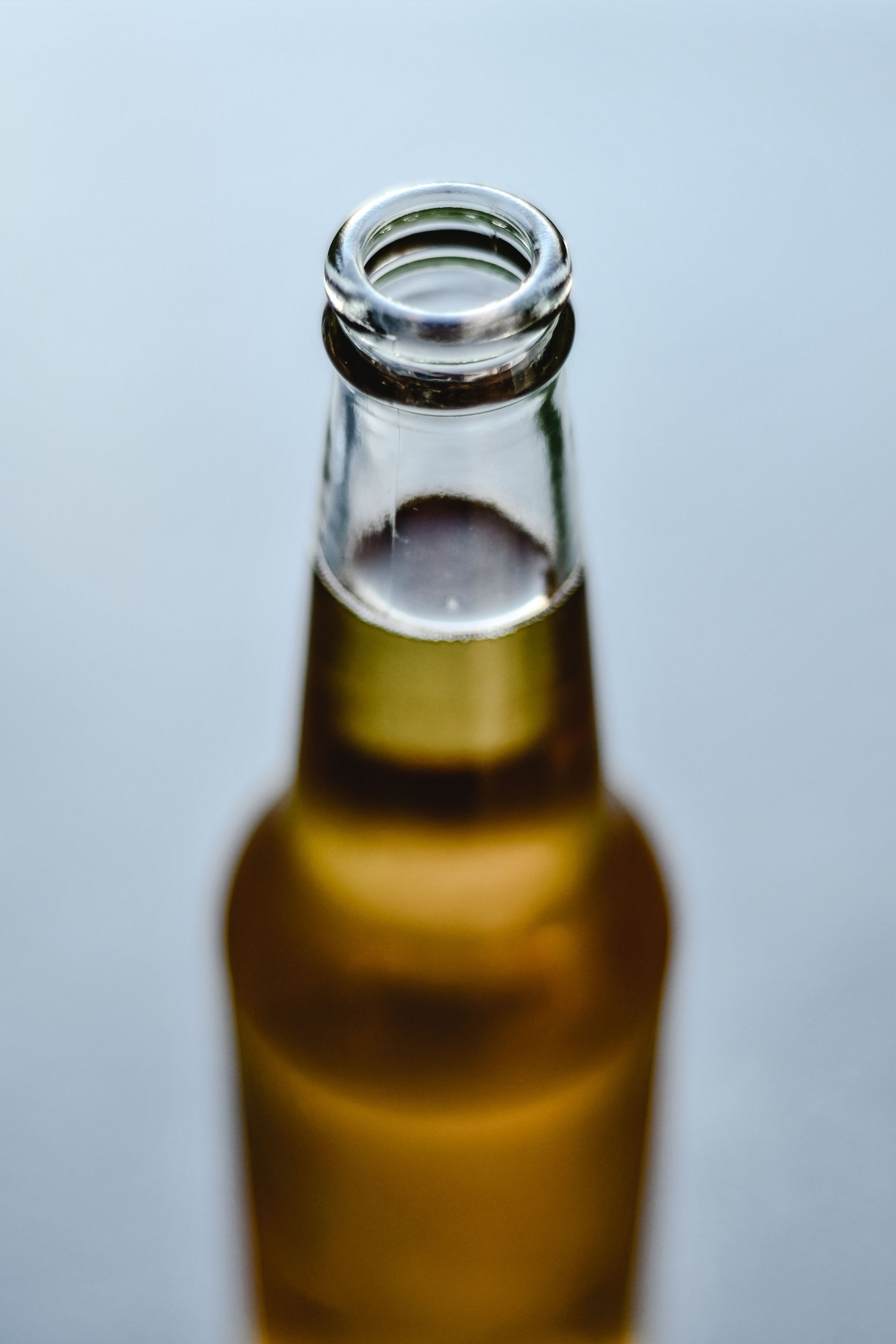 Glass beer bottle with focus on the neck and blurred background, emphasizing its amber color.