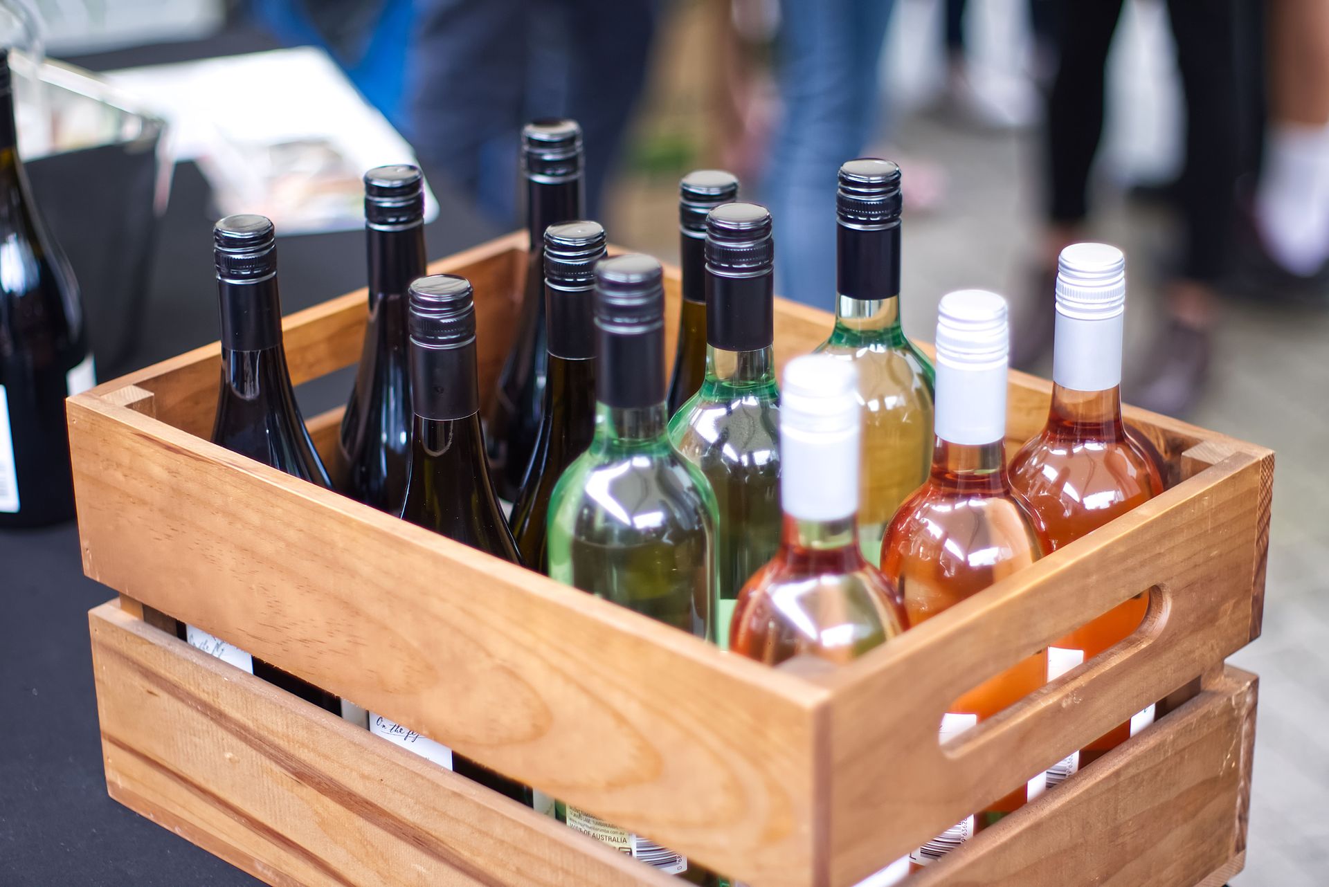 A wooden crate filled with diverse wine bottles at an outdoor gathering.